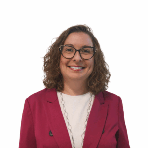 A woman with curly brown hair wearing glasses, a magenta blazer, a white top, and a long necklace, smiling at the camera against a plain white background.