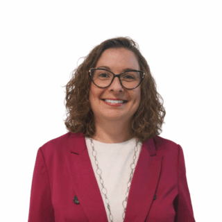 A woman with curly brown hair wearing glasses, a magenta blazer, a white top, and a long necklace, smiling at the camera against a plain white background.