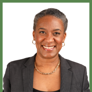 A smiling person with short gray hair, wearing a black blazer, a black top, and a gold necklace and hoop earrings, is in the center of the image, set against a plain white background with a green border.