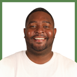 A man with short hair and a beard is smiling while wearing a white shirt. The background is white with a green border.