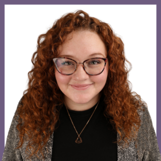 A person with curly red hair and glasses smiles at the camera. They are wearing a black top, a patterned cardigan, and a geometric necklace against a white background with a purple border.