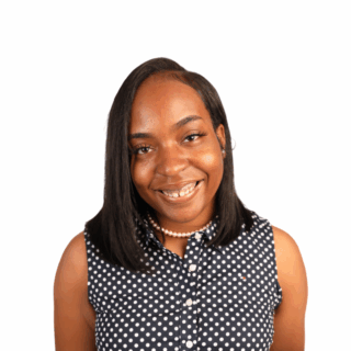 A woman with straight black hair, wearing a sleeveless navy blue polka dot top and a pearl necklace, smiles at the camera against a white background.