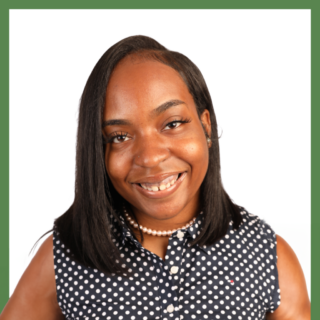 A person with shoulder-length black hair smiles at the camera. They are wearing a sleeveless navy blue polka dot shirt and a pearl necklace. The background is plain white with a green border.