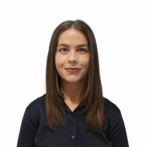 A young woman with straight brown hair, wearing a black button-up shirt, is standing against a plain white background, smiling softly at the camera.