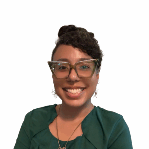 A smiling person with curly hair, wearing large, angular glasses and a green top, poses against a plain white background.