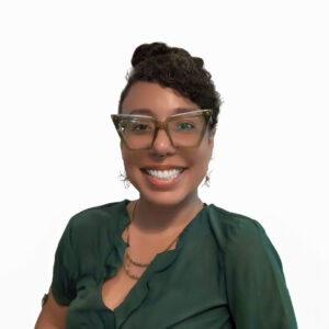 A smiling woman with curly hair up, wearing large glasses, earrings, a green blouse, and a layered necklace, posed against a plain white background.