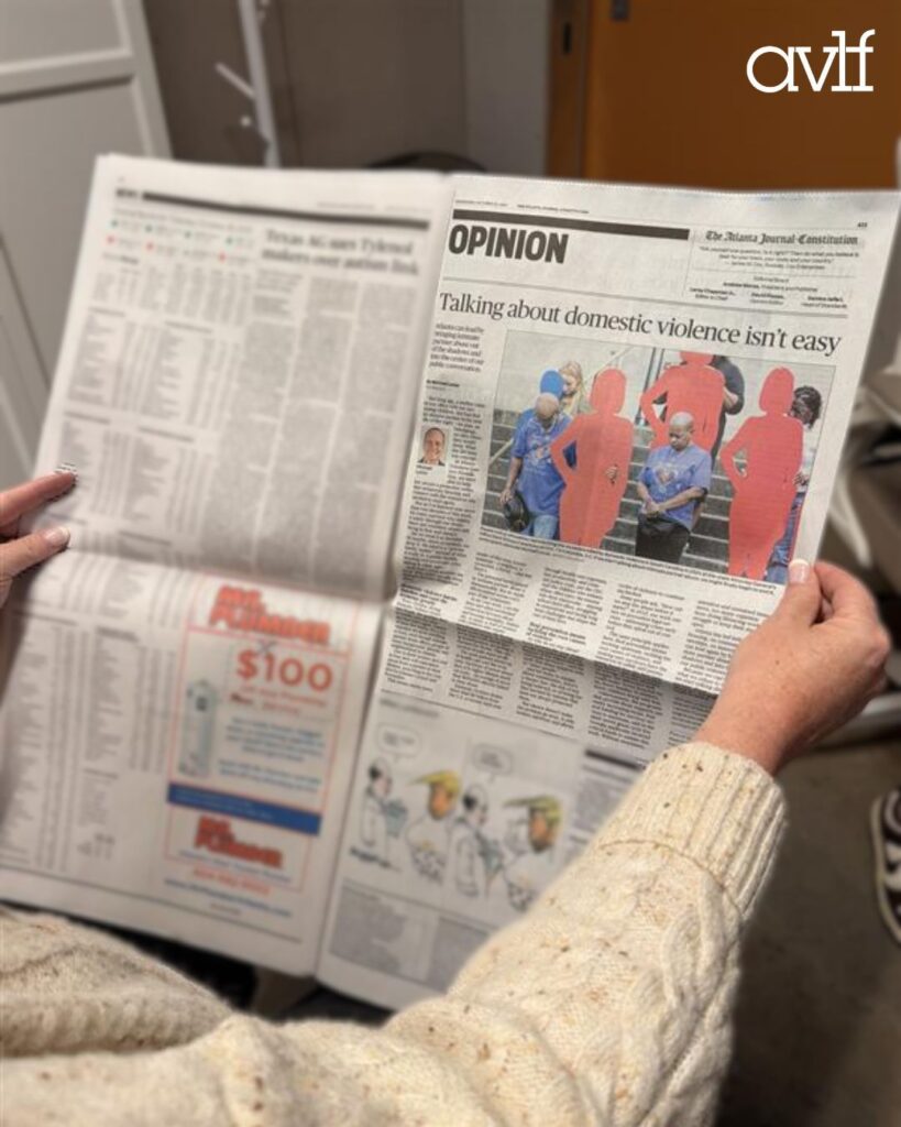 A person wearing a cream sweater holds a newspaper opened to an opinion article titled "Talking about domestic violence isn't easy," featuring an image of people with some figures filled in red.