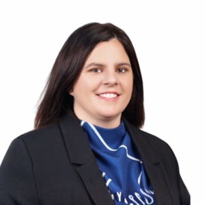 A woman with straight dark brown hair, wearing a black blazer and a blue patterned scarf, is smiling against a plain white background.