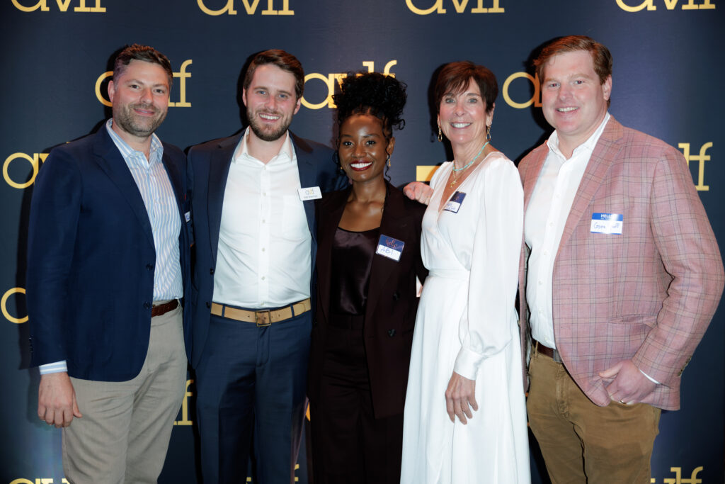 Five people stand together smiling at an event, dressed in business or cocktail attire, in front of a blue backdrop with yellow "CMF" logos.