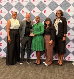 Five people standing together and smiling in front of a HouseATL step-and-repeat banner, with the person in the center holding a glass award.