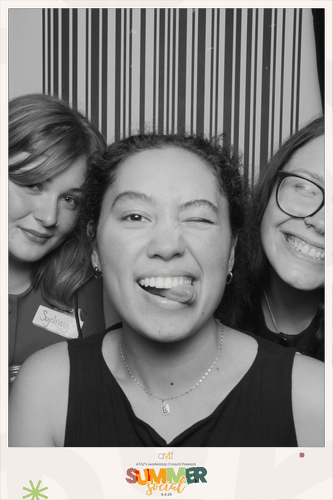 Three young people smile and pose playfully for a black-and-white photo. The person in the center winks and sticks out their tongue, while the two others stand close on either side in front of a striped background.