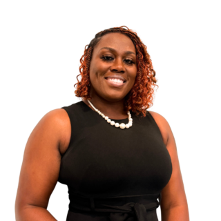 A woman with curly auburn hair, wearing a sleeveless black dress and a pearl necklace, smiles confidently against a plain white background.