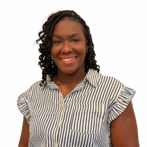 A woman with curly hair smiles at the camera. She is wearing a blue and white striped short-sleeve blouse with ruffled shoulders, and stands against a plain white background.