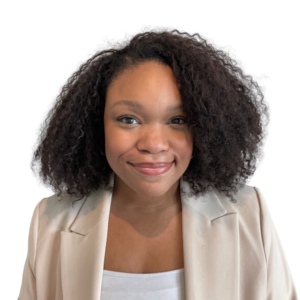 A woman with curly dark hair smiles at the camera. She is wearing a light-colored blazer over a white top and is posed against a plain white background.