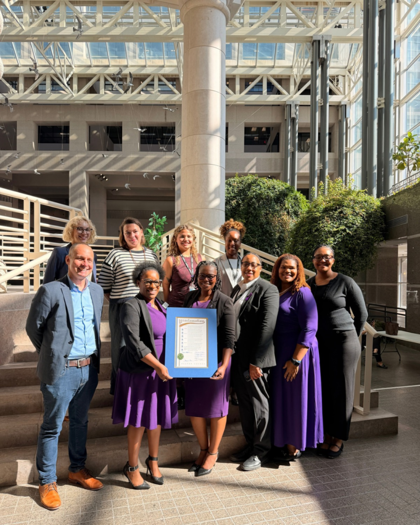 A group of ten people posing for a photo on stairs, with two people in the center holding a framed proclamation document.